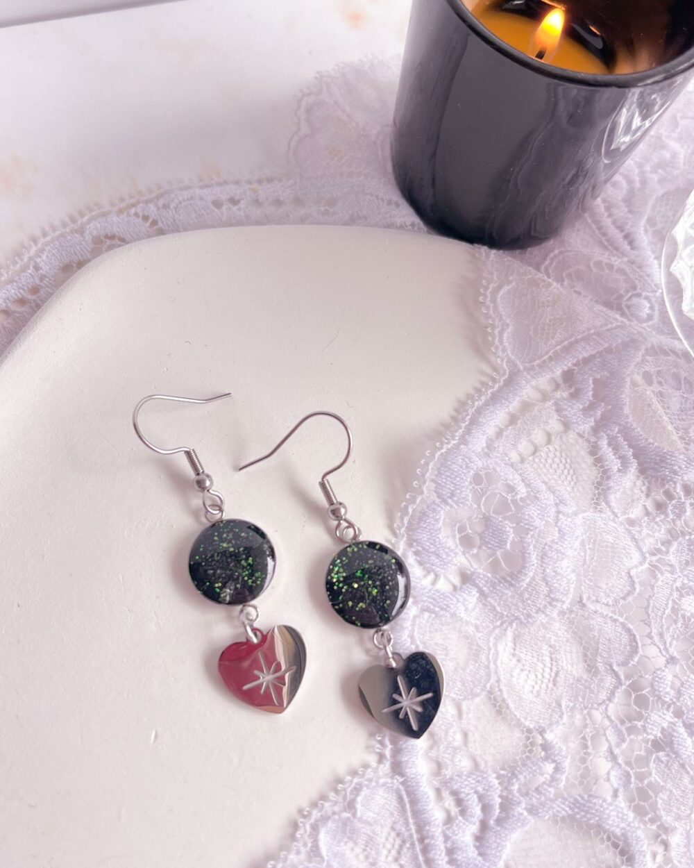 Boucles argentées en acier inoxydable avec médaillon noir de 12 mm incrusté de sable d’aventurine verte et breloque cœur contenant une étoile ajourée.