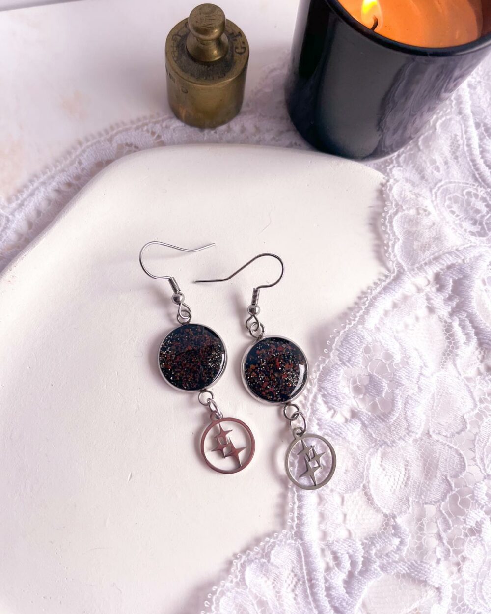 Boucles d’oreilles argentées en acier inoxydable avec médaillon noir en argile polymère incrusté de sable de jaspe rouge et breloque étoile.