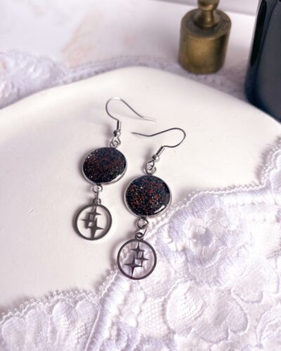 Boucles d’oreilles argentées en acier inoxydable avec médaillon noir en argile polymère incrusté de sable de jaspe rouge et breloque étoile.