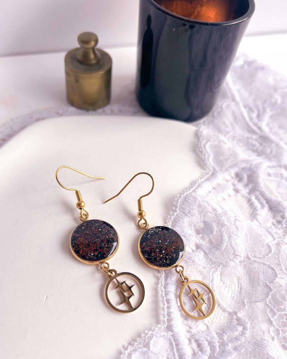 Boucles d’oreilles dorées en acier inoxydable avec médaillon noir en argile polymère serti de sable de jaspe rouge et breloque étoile.