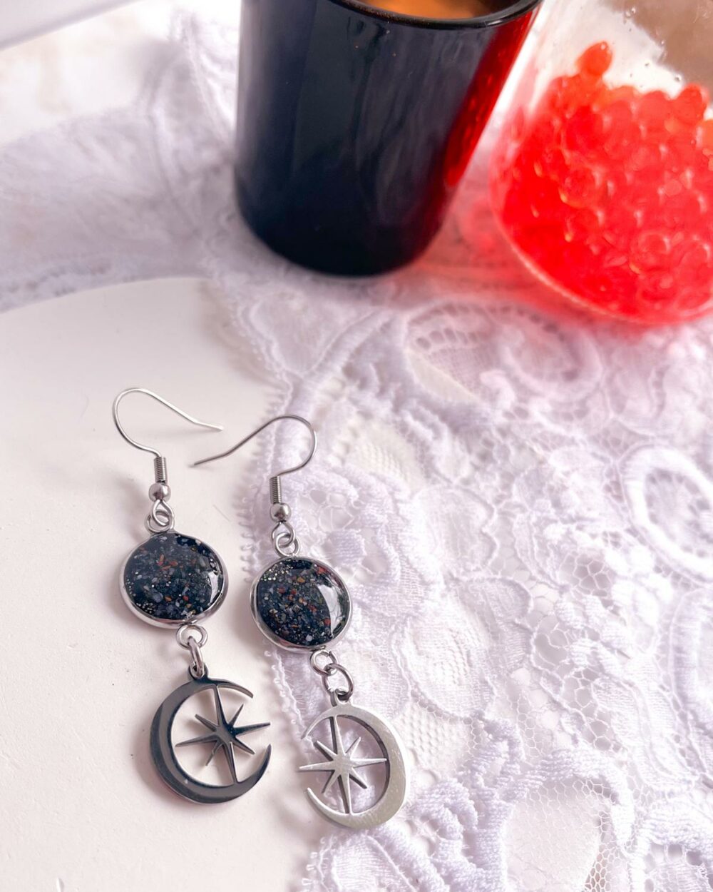 Boucles argentées en acier inoxydable avec médaillon noir de 12 mm incrusté de sable de cornaline et breloque lune avec étoile au centre.