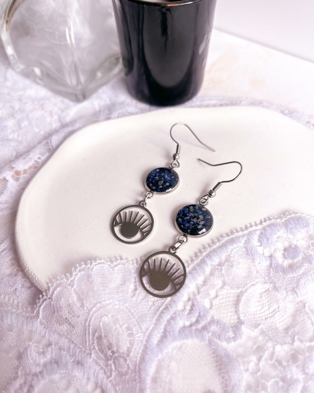 Boucles argentées en acier inoxydable avec médaillon noir de 12 mm incrusté de sable de lapis-lazuli et breloque œil dans rond ajouré.